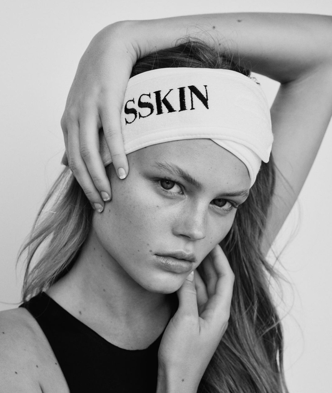 A black and white image of a young woman in a black tank top wearing a protective hair band with the SSKIN brand logo